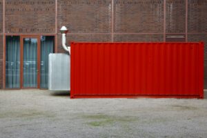 Röd avfallscontainer placerad vid tegelbyggnad – exempel på containerlösning i stadsmiljö