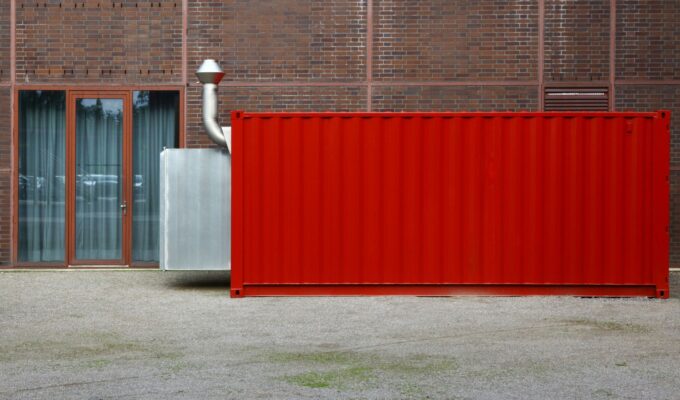 Röd avfallscontainer placerad vid tegelbyggnad – exempel på containerlösning i stadsmiljö